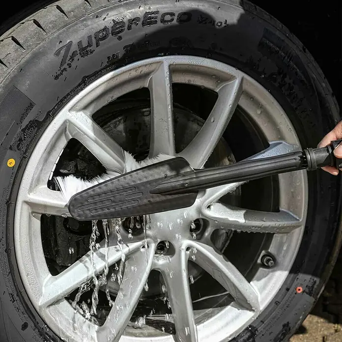 Scheppach Hochdruckreiniger HPC1600-Kit - 135 bar, 1.600 W, Fördermenge: 420 l/h - Ein Autorad wird mit einem Bürstenaufsatz und Wasser gereinigt, wodurch das saubere, silberne Felgendesign sichtbar wird.