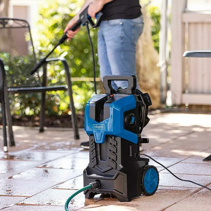Scheppach Hochdruckreiniger HCE3000 - 2.400 W, Fördermenge: 480 l/h, 180 bar - Der Scheppach Hochdruckreiniger HCE1600 im Einsatz beim Reinigen einer Terrasse. Das Gerät ist kompakt, blau und schwarz.