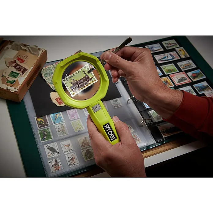 Ryobi 4V USB Akku-Lupenleuchte RML4-120G - 4 V, 1 Akku, 2 Ah - Das Bild zeigt eine Lupe der Marke Ryobi, die dazu verwendet wird, eine Briefmarke mit einem Zugmotiv zu betrachten.