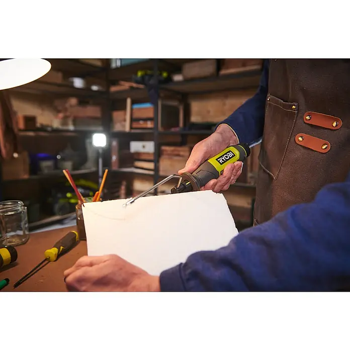 Ryobi 4V USB Akku-Heißdrahtschneider RHC4 - 4 V, 1 Akku, 2 Ah - Nahaufnahme einer Person, die mit einem Ryobi-Werkzeug ein Stück Styropor bearbeitet, im Hintergrund Werkzeuge und Regale.