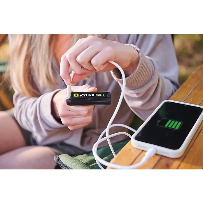 Ryobi 4V USB Akku RB4L30 - 4 V, 3 Ah - Eine Person, die ein Ryobi USB Lithium-Ladegerät verwendet, um ein Smartphone mit vollem Akku aufzuladen. Kompakte Stromversorgung für unterwegs.