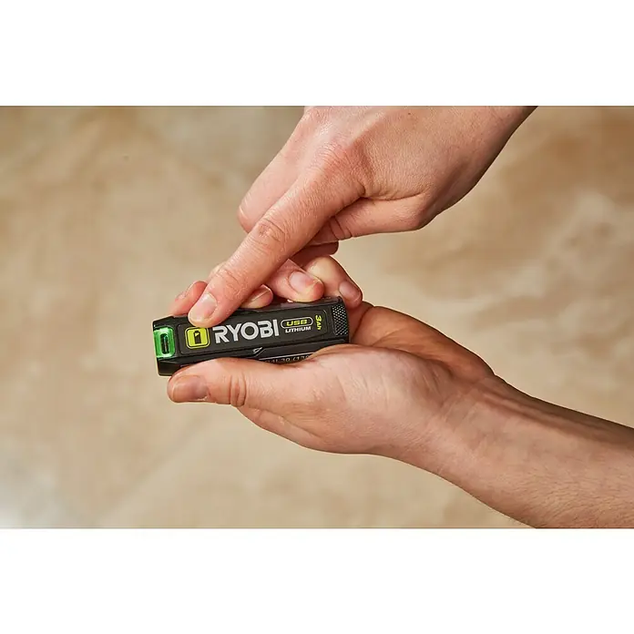 Ryobi 4V USB Akku RB4L30 - 4 V, 3 Ah - Nahaufnahme einer Hand, die einen schwarzen Ryobi USB Lithium Akku hält, mit dem Fokus auf das Produkt, welches eine grüne LED-Anzeige besitzt.