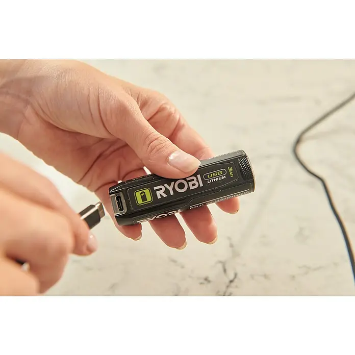 Ryobi 4V USB Akku RB4L30 - 4 V, 3 Ah - Das Bild zeigt einen Ryobi USB-Lithium-Akku, der an ein Ladekabel angeschlossen wird. Der Akku ist kompakt und für verschiedene Geräte geeignet.