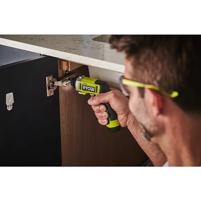 Ryobi 4V USB Akkuschrauber RSD4-120TA2 - 4 V, 1 Akku, 5 Nm - Nahaufnahme eines Mannes, der mit einem Ryobi-Akkuschrauber ein Scharnier an einem Schrank befestigt.