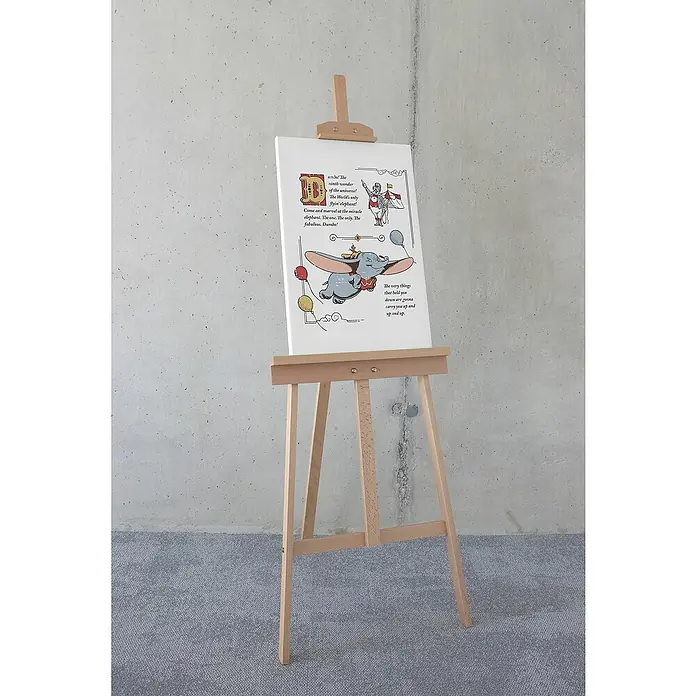 Komar Dumbo Leinwandbild - Dumbo the Flying Elephant, B x H: 40 x 60 cm - Nahaufnahme eines Holzstaffelei-Displays mit einer charmanten Dumbo-Illustration, die die skurrile Ästhetik des Produkts hervorhebt.