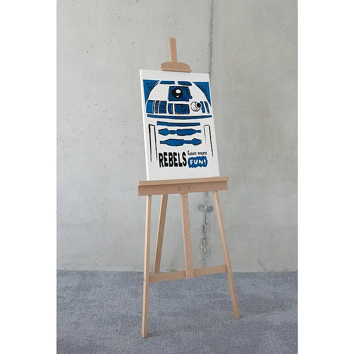 Komar Star Wars Leinwandbild - Star Wars R2D2 More Fun, B x H: 40 x 60 cm - Das Bild zeigt ein R2-D2-Poster auf einer Staffelei, das mit den Worten "Rebels have more fun!" beschriftet ist. Das Star Wars-Artwork ist im Pop-Art-Stil gehalten.