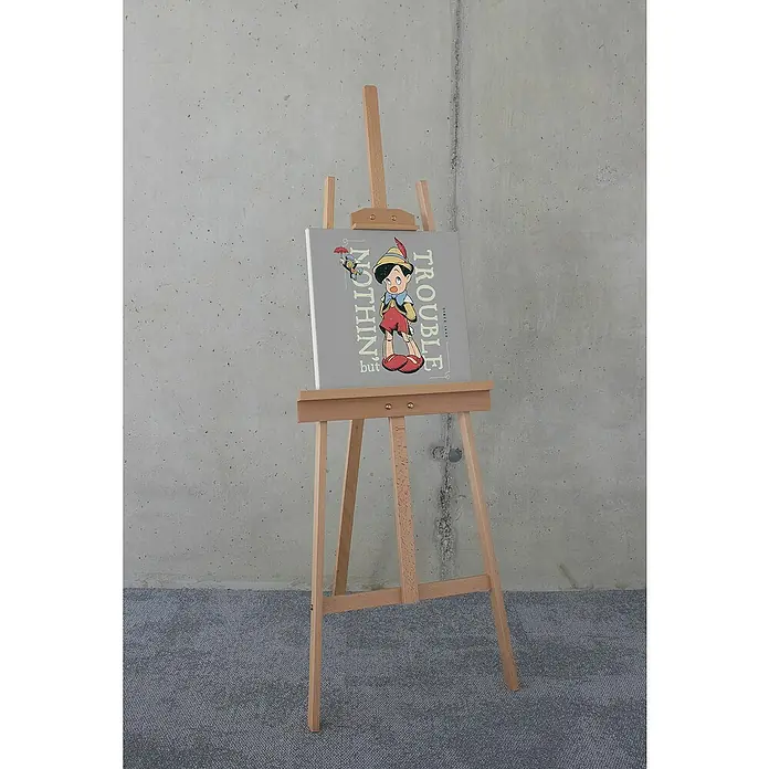 Komar Leinwandbild - Hey Pinocchio, B x H: 40 x 40 cm - Eine Nahaufnahme einer Staffelei mit einem Leinwandbild von Pinocchio mit dem Text "Nichts als Ärger seit 1940".