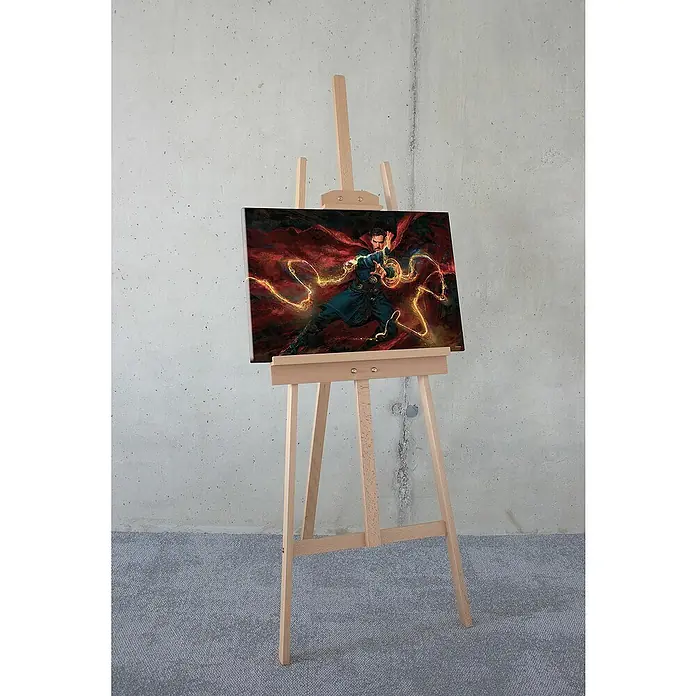 Komar Leinwandbild - Doctor Strange Sorcerer Supreme, B x H: 60 x 40 cm - Ein gerahmtes Doctor Strange-Gemälde steht auf einer hölzernen Staffelei vor einer Betonwand und einem grauen Teppich.