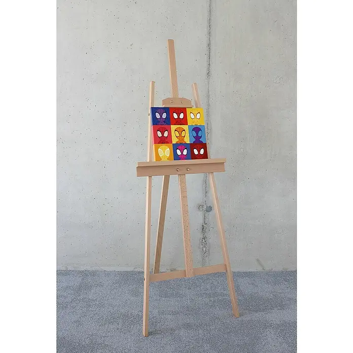 Komar Leinwandbild - Spidey Symmetry, B x H: 30 x 30 cm - Nahaufnahme einer Leinwand mit Spider-Man-Illustrationen auf einer Holzstaffelei vor einer Betonwand, präsentiert ein farbenfrohes Pop-Art-inspiriertes Kunstwerk.