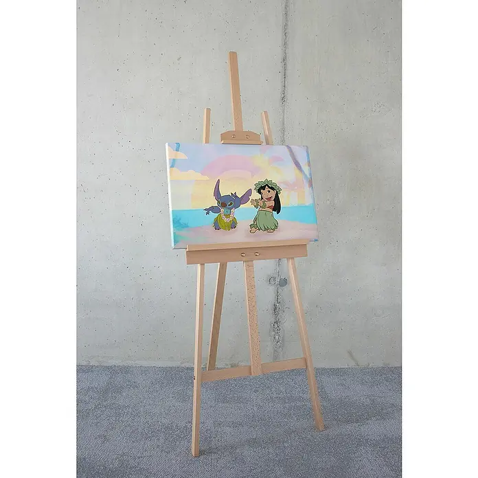 Komar Leinwandbild - Lilo and Stitch Dancing, B x H: 60 x 40 cm - Das Bild zeigt eine Leinwand mit einem bunten Gemälde von Lilo und Stitch auf einer Staffelei vor einer grauen Wand und einem grauen Teppich.