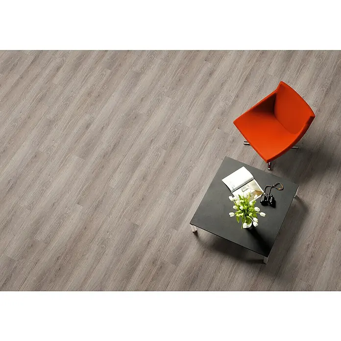 LOGOCLIC Laminado Roble Hiedra - 1.380 x 193 x 7 mm, AC5 - Elegante suelo laminado gris con una sutil textura de madera, combinado con un moderno sillón naranja y una mesa de centro negra.