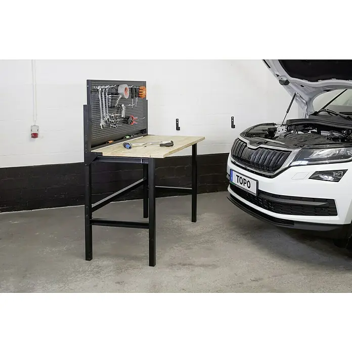 Werkbank Klappbar - L x B: 64,6 x 121,5 cm, Arbeitshöhe: 142 cm, Belastbarkeit: 150 kg - Werkbank mit Werkzeugwand neben einem Auto. Die Werkbank bietet Arbeitsfläche und Aufbewahrung für Werkzeuge.