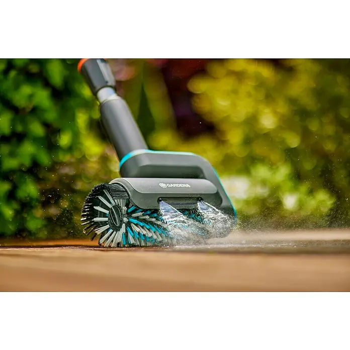 Gardena Power for All 18V Akku-Reinigungsbürste AquaBrush Patio 03/18V - 1 Akku - Eine rotierende Bürste von Gardena mit Wasserstrahl reinigt eine Holzterrasse. Die Bürste hat blaue Akzente.
