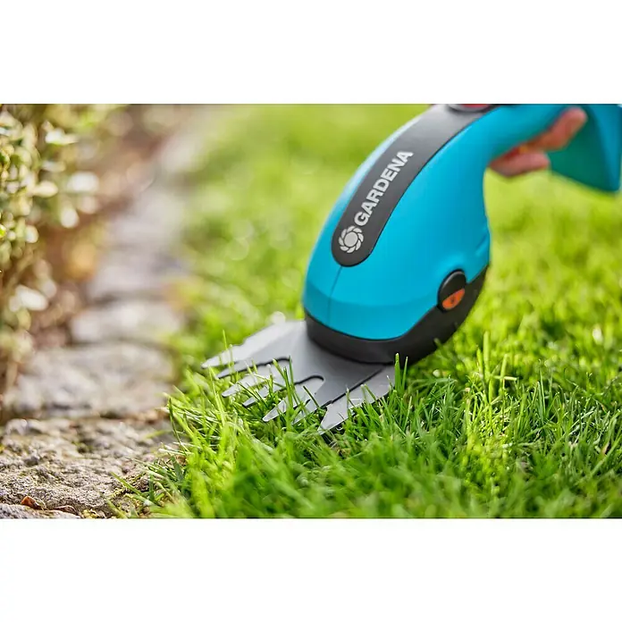 Gardena Power for All 18V Akku-Gras- & Strauchschere 20/18V P4A - 18 V, Li-Ionen, Ohne Akku - Nahaufnahme einer Gardena Akku-Grasschere beim Trimmen von Gras entlang eines Steinpfads. Ideal zum präzisen Kantenschneiden im Garten.
