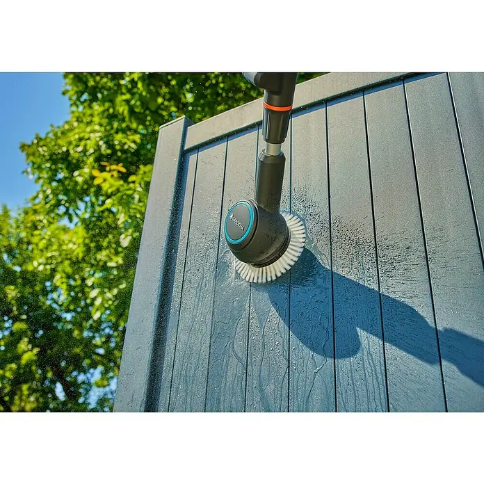 Gardena Power for All 18V Akku-Reinigungsbürste AquaBrush Compact 02/18V - Ohne Akku - Das Bild zeigt eine GARDENA Bürste, die eine graue Holzoberfläche reinigt und Wasser spritzt. Ideal für die Gartenpflege und Reinigung im Außenbereich.