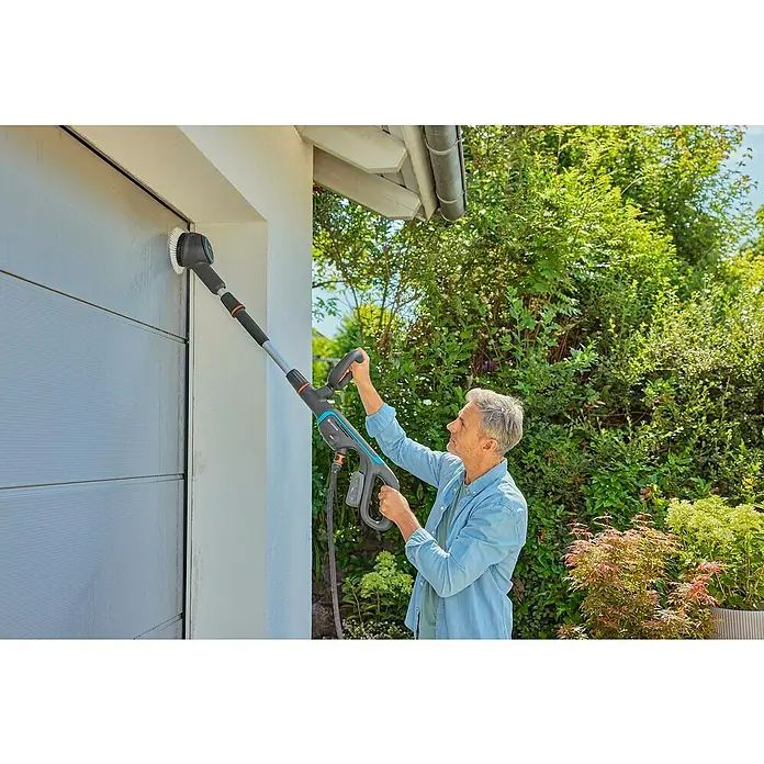 Gardena Power for All 18V Akku-Reinigungsbürste AquaBrush Compact 02/18V - Ohne Akku - Mann benutzt eine GARDENA Reinigungsbürste an einer Garagenwand. Die Bürste ist an einem Teleskopstiel befestigt für schwer erreichbare Stellen.