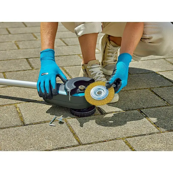 Gardena Power for All 18V Limpiador de juntas de batería EasyWeed 1800/18V - 18 V, 1 batería - Primer plano de una mujer que utiliza un cepillo para juntas a batería GARDENA con un cepillo de alambre para eliminar las malas hierbas de las juntas de pavimentación.