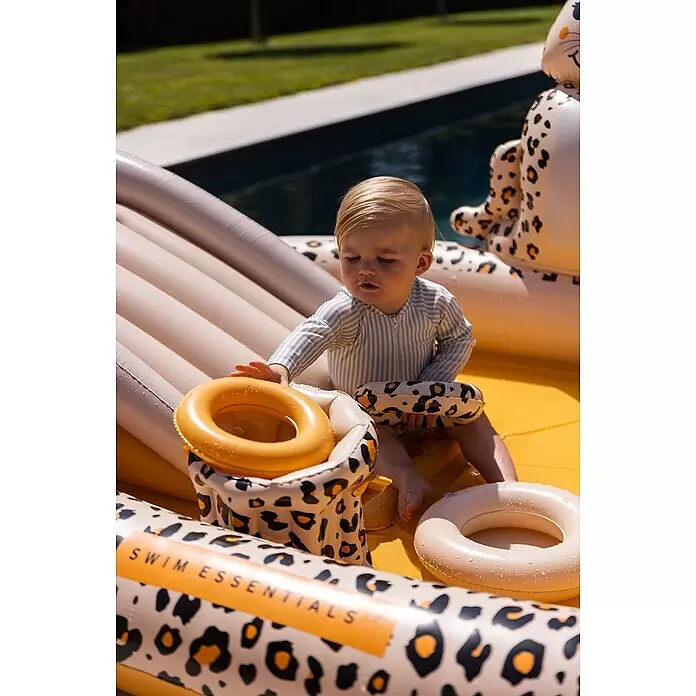 Swim Essentials Piscina hinchable - 203 x 173 x 89 cm, Leopardo - Bebé en bañador a rayas juega en un tobogán de piscina inflable amarillo con estampado de leopardo y anillos naranjas.