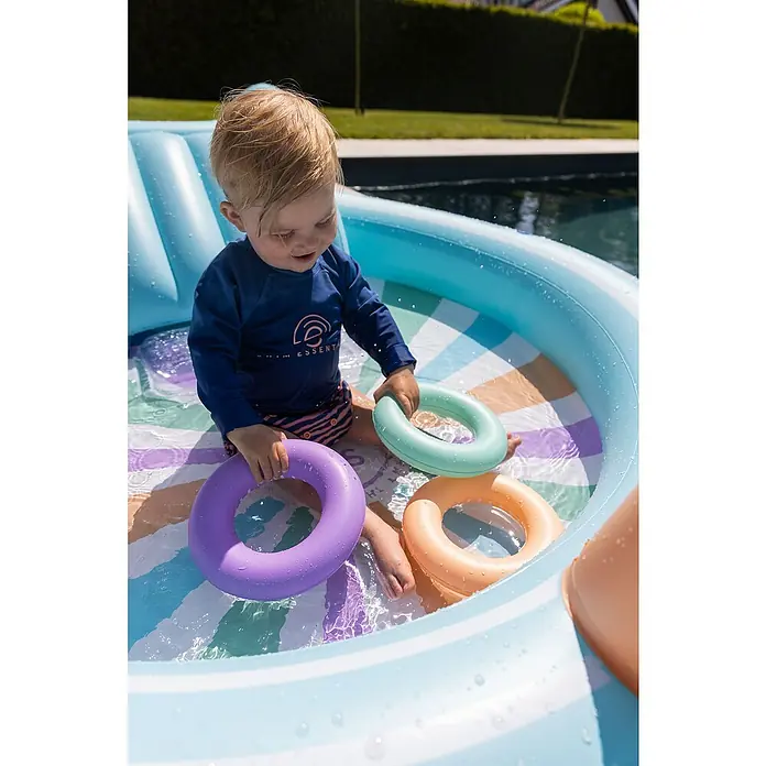 Swim Essentials Planschbecken - 203 x 173 x 89 cm, Regenbogen - Ein Kleinkind spielt im Planschbecken mit bunten Spielringen, ein fröhlicher Moment im Freien. Das Schwimmbecken bietet spass und Abkühlung.