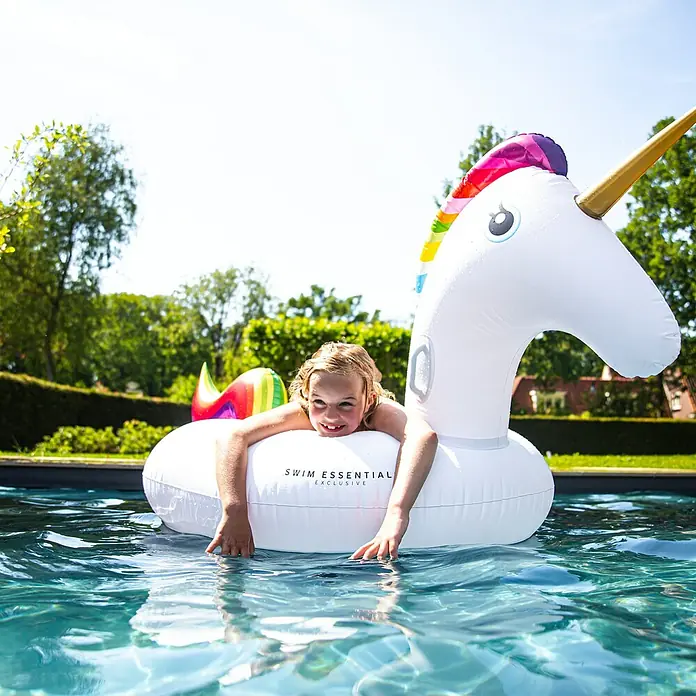 Swim Essentials Schwimmtier Einhorn - 142 x 137 x 97 cm - Ein junges Mädchen entspannt auf einem aufblasbaren, weißen Einhorn-Schwimmtier der Marke Swim Essential im Pool.