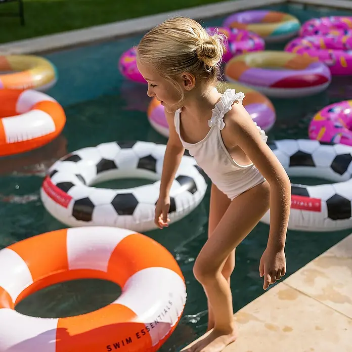 Swim Essentials Schwimmring - Durchmesser: 90 cm, Fussball - Mädchen am Pool mit Swim Essentials Schwimmreifen in Orange und Weiß, sowie Fußball-Design. Spaß im Wasser mit den farbenfrohen Schwimmhilfen.