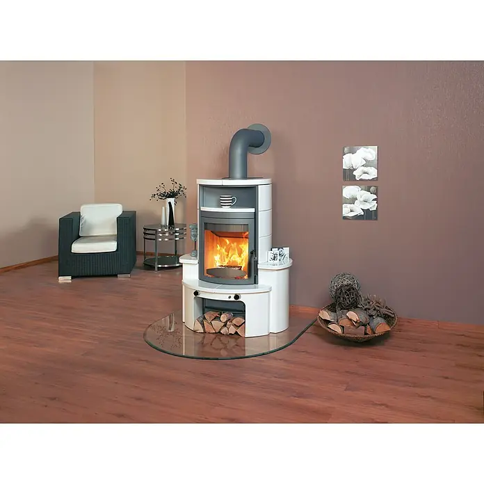 Hark Kaminofen Avenso GT ECOplus - 6 kW, Raumheizvermögen: 165 m³, Material Verkleidung: Keramik, Weiß/Creme - Ein Kaminofen mit Holzscheiten darunter und einem runden Glasboden davor, daneben ein Korb mit weiteren Holzscheiten zur Dekoration.