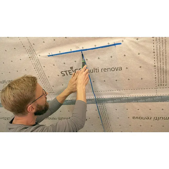 Steico Dampfbremsfolie multi renova - 50 x 1,5 m, 75 m² - Ein Mann schneidet mit einem Messer die Steico multi renova Dampfbremsbahn, eine feuchtevariable Dampfbremsmembran, zu.