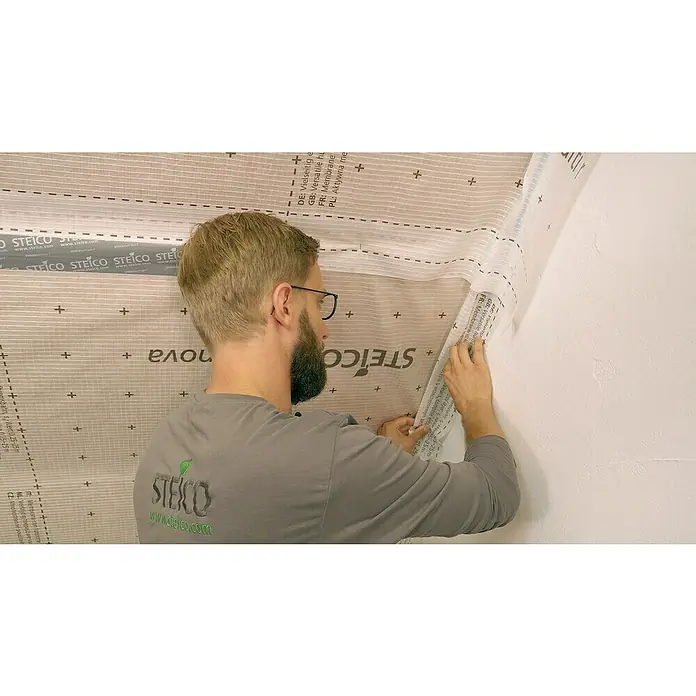 Steico Klebe- & Dichtmasse multi connect - Modifizierte Dispersion - Ein Mann befestigt eine STEICO Membran an einer Wand, die für ihre vielseitige, feuchtigkeitsregulierende und luftdichte Funktion bekannt ist.