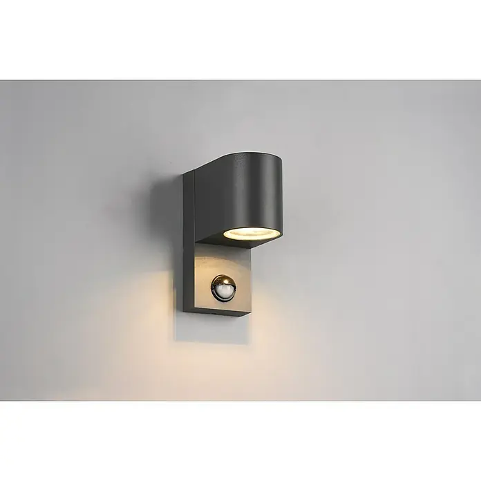 Trio Leuchten Außenwandleuchte ROYA - 35 W, L x B x H: 11,6 x 7 x 15 cm, Grau, IP44 - Nahaufnahme einer modernen, anthrazitfarbenen LED-Außenwandleuchte mit Bewegungsmelder an einer grauen Wand, die ein warmes Licht ausstrahlt.