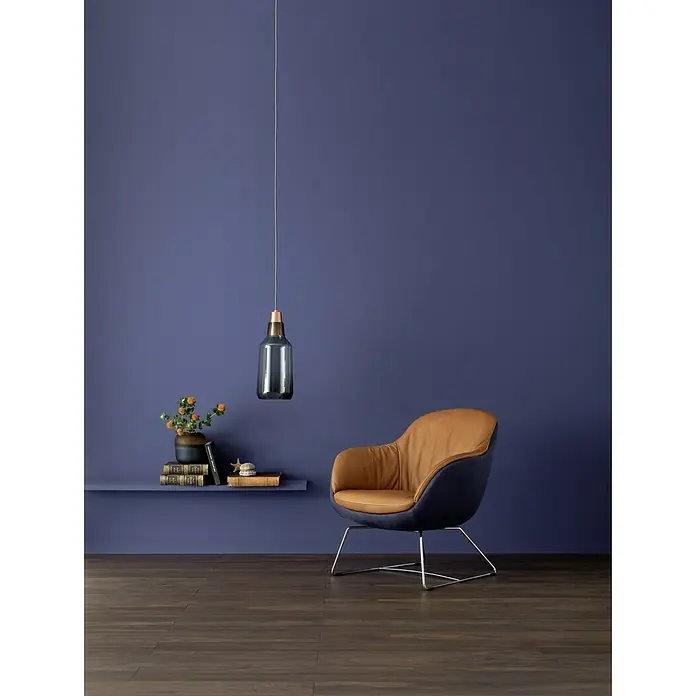 SCHÖNER WOHNEN-Farbe Wandfarbe Designfarbe - Unendliches Tiefseeblau, Matt, 2,5 l, Konservierungsmittelfrei - Elegante Inneneinrichtung mit einem modernen Sessel in Braun und Blau, einer stilvollen Lampe und einem Bücherregal an einer violetten Wand.
