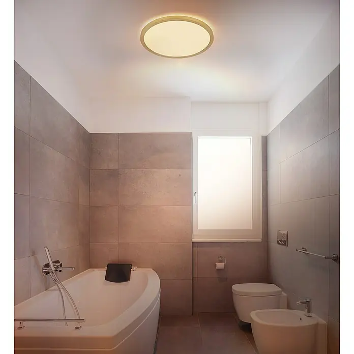 Globo LED-Deckenleuchte rund Sapana - 18 W, Warmweiß, Messing, Ø x H: 29,4 cm x 25 mm - Die runde Deckenleuchte in Goldfarben wirft ein warmes Licht in das Badezimmer mit grauen Fliesen und weißer Badewanne.