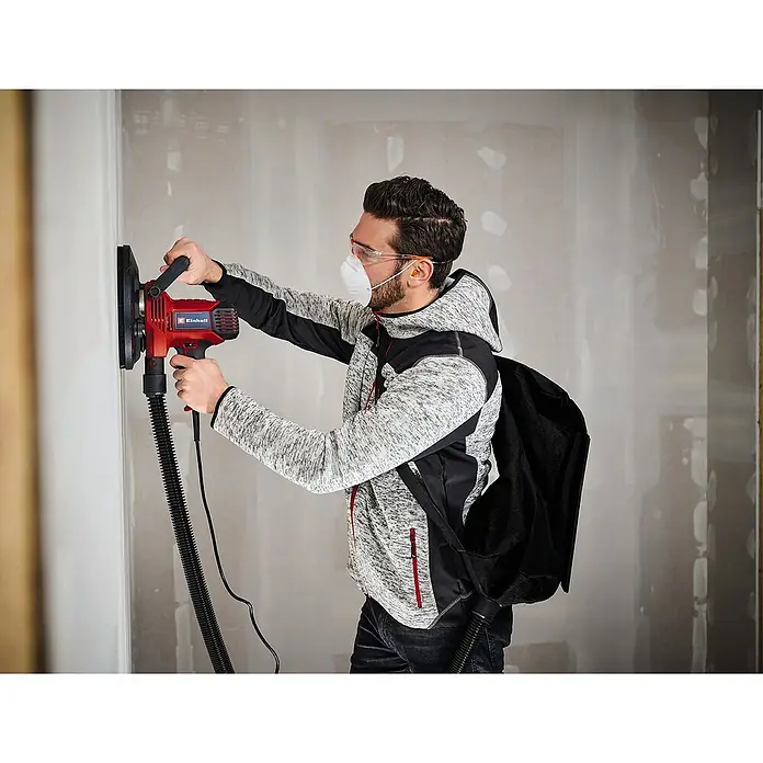 Einhell Trockenbauschleifer TC-DWS 225 - 1.220 W, Durchmesser Schleifteller: 215 mm, Leerlaufdrehzahl: 1.500 U/min - 2.300 U/min - Ein Mann schleift mit einem Einhell Mauerschleifer eine Wand, um sie für die weitere Bearbeitung vorzubereiten. Staub wird abgesaugt.