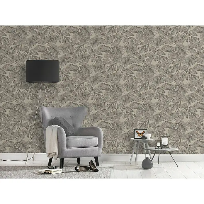 A.S. Création Casual Living Vliestapete - Braun/Grau/Beige, Floral, 10,05 x 0,53 m - Einladendes Wohnzimmer mit grauem Sessel, Stehlampe und Beistelltischen vor einer auffälligen Blättertapete.