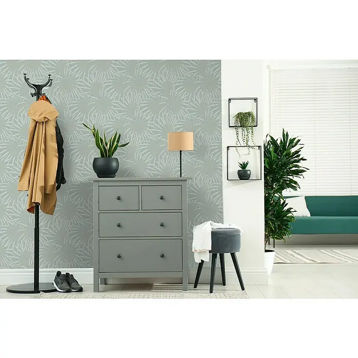 A.S. Création Casual Living Vliestapete Palmenblätter - Blau/Mint, Floral, 10,05 x 0,53 m - Elegante graue Kommode mit Dekorationen wie Pflanzen und einer Lampe, die eine stilvolle Atmosphäre im Raum schafft.
