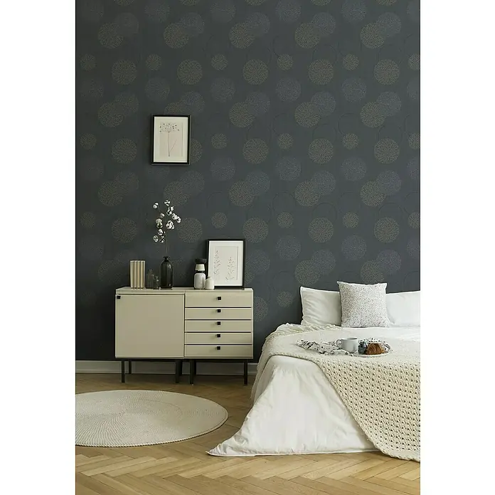 A.S. Création Casual Living Vliestapete Kreise - Anthrazit-Grau, Grafisch, 10,05 x 0,53 m - Einrichtung eines Schlafzimmers mit einem hellen Nachttisch, einem Bett mit weißer Bettwäsche und einem runden Teppich auf hellem Holzboden.