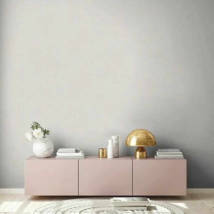 A.S. Création Casual Living Vliestapete - Grau/Hellgrau, Uni, 10,05 x 0,53 m - Elegante Inneneinrichtung mit einem rosa Sideboard, verziert mit einer goldenen Lampe, Büchern und einer Blumenvase.
