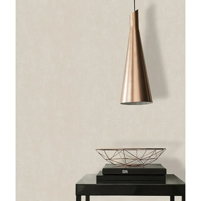 A.S. Création Casual Living Vliestapete - Harmonisches Beige, Uni, 10,05 x 0,53 m - Moderne Raumgestaltung mit einer eleganten Kupferpendelleuchte, die über einem schwarzen Tisch mit Deko-Objekten hängt.