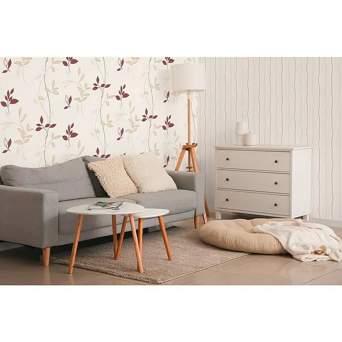 A.S. Création Casual Living Vliestapete Blätter - Creme/Rot/Beige, Floral, 10,05 x 0,53 m - Eine gemütliche Wohnzimmereinrichtung mit einem grauen Sofa, einem weißen Couchtisch und einem beigen Bodenkissen, die eine einladende Atmosphäre schaffen.