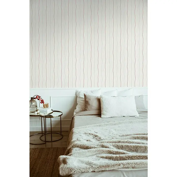 A.S. Création Casual Living Vliestapete - Creme/Rot, Streifen, 10,05 x 0,53 m - Schlafzimmer mit Bett und Nachttisch vor einer Wand mit Tapete mit geschwungenen Streifen.