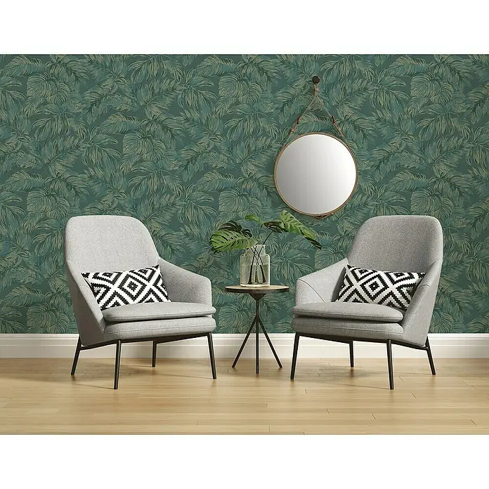 A.S. Création Casual Living Vliestapete - Grün/Gold, Floral, 10,05 x 0,53 m - Zwei graue Sessel mit Kissen und einem Beistelltisch auf einem Holzboden vor einer grünen Blättertapete.