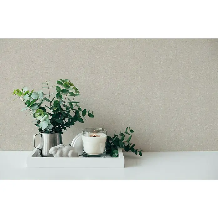 A.S. Création Casual Living Vliestapete - Harmonisches Beige, Uni, 10,05 x 0,53 m - Stillleben mit einer Kerze im Glas, einem silbernen Becher mit Eukalyptus und einer kleinen Hasenfigur auf einem weißen Tablett.