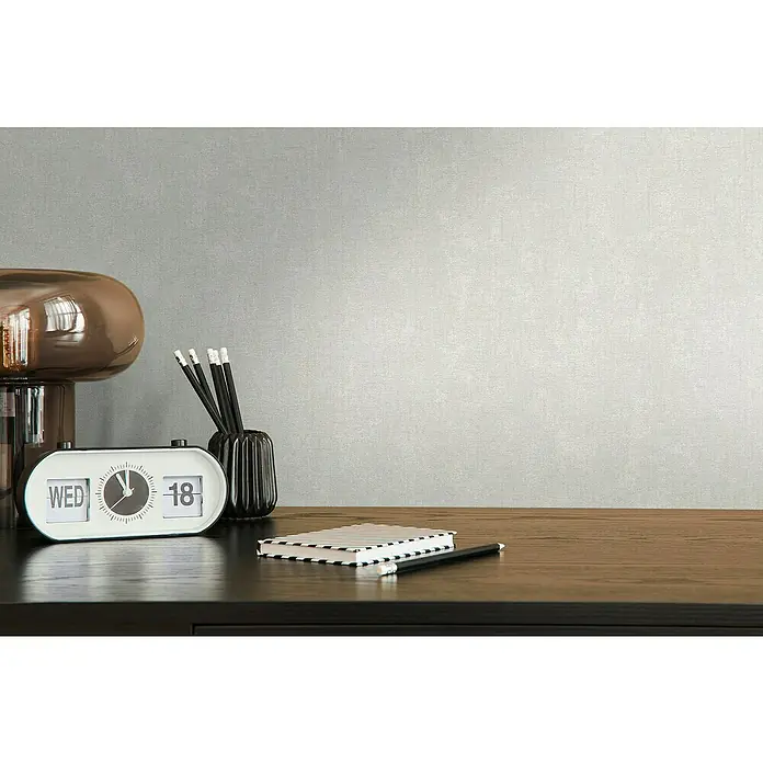 A.S. Création Casual Living Vliestapete - Helles Grau, Uni, 10,05 x 0,53 m - Nahaufnahme eines Tisches mit einer Lampe, einer Uhr, Stiften und einem Notizblock.