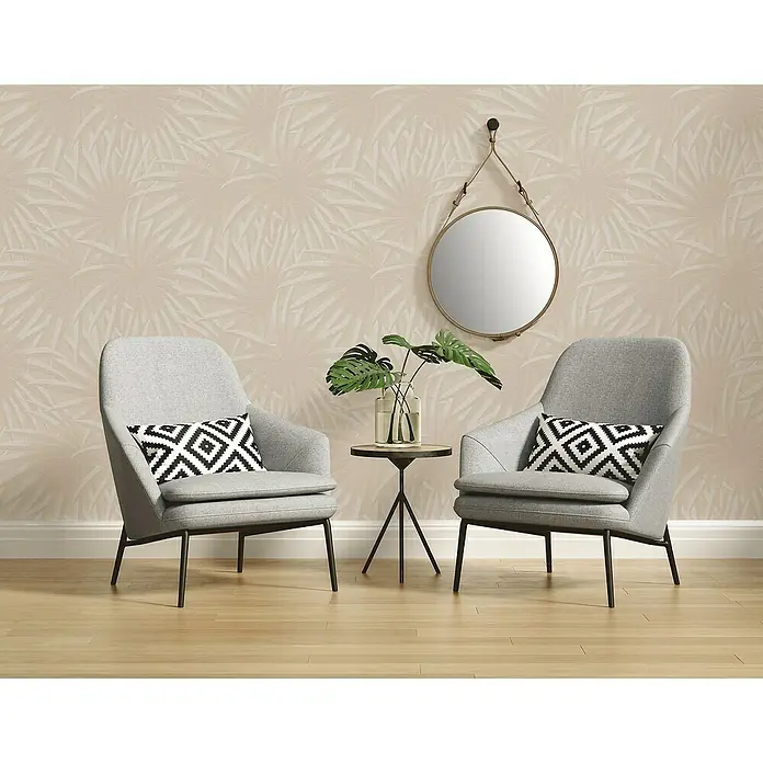 A.S. Création Casual Living Vliestapete Palmenblätter - Beige/Weiß, Floral, 10,05 x 0,53 m - Einladende Leseecke mit zwei grauen Sesseln, Akzentkissen, kleinem Beistelltisch und einem runden Spiegel an einer gemusterten Wand.