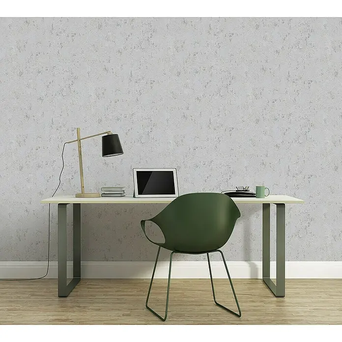 A.S. Création Casual Living Vliestapete Struktur - Grau/Silber/Metallic, Uni, 10,05 x 0,53 m - Eine elegante Arbeitsplatzeinrichtung mit einer minimalistischen Schreibtischlampe, einem Tablet und einem bequemen Stuhl vor einer strukturierten Wand.