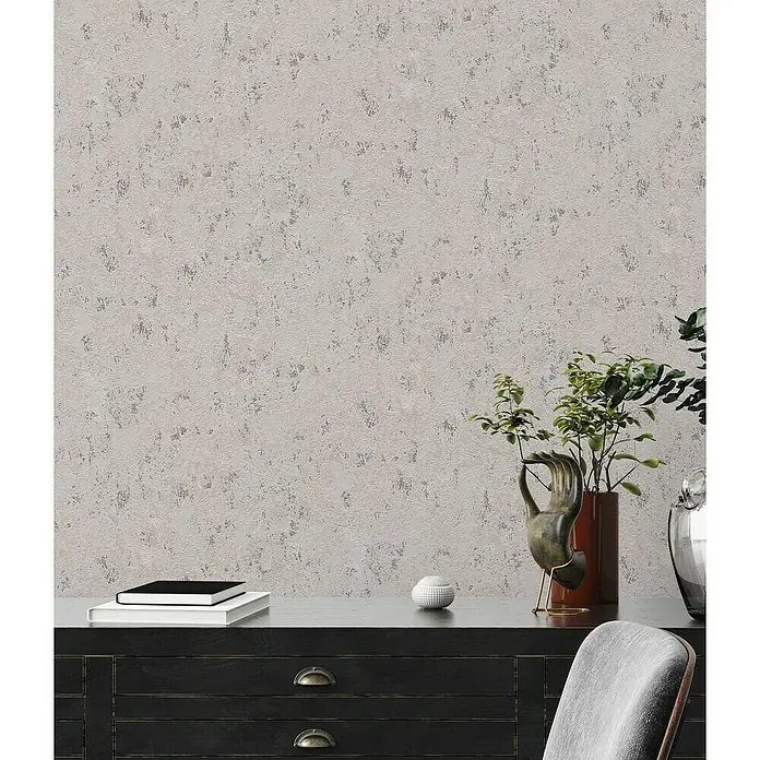 A.S. Création Casual Living Vliestapete Struktur - Grau/Beige/Silber, Uni, 10,05 x 0,53 m - Nahaufnahme einer modernen Inneneinrichtung mit einer Kommode, Büchern, Pflanzen und einer auffälligen Wandstruktur.