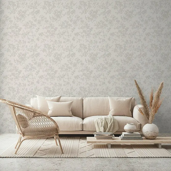 A.S. Création Casual Living Vliestapete Blümchen - Weiß/Grau, Floral, 10,05 x 0,53 m - Beige Couch mit Kissen und Holztisch, dekoriert mit Vasen und Büchern, vor einer Wand mit floralem Muster. Gemütliche Wohnraumgestaltung.