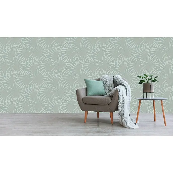 A.S. Création Casual Living Vliestapete Palmenblätter - Blau/Mint, Floral, 10,05 x 0,53 m - Einrichtungsidee mit bequemen Sessel, Beistelltisch und Grünpflanze vor einer grünen gemusterten Tapete.