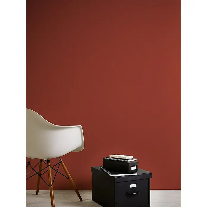 A.S. Création Casual Living Vliestapete - Rot, Uni, 10,05 x 0,53 m - Ein minimalistisches Interieur mit einem eleganten, weißen Stuhl und schwarzen Aufbewahrungsboxen vor einer warmen, terrakottafarbenen Wand.