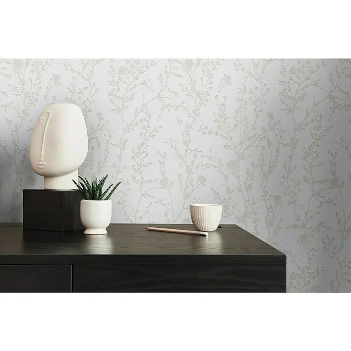 A.S. Création Casual Living Vliestapete - Hellgrau/Weiß, Floral, 10,05 x 0,53 m - Nahaufnahme eines stilvollen Schreibtisches mit einer modernen Skulptur, einer kleinen Pflanze und einer minimalistischen Tasse vor einer floralen Tapete.