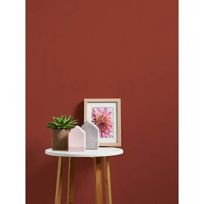 A.S. Création Casual Living Vliestapete - Rot, Uni, 10,05 x 0,53 m - Dekorative Tischszene mit einer Sukkulente, kleinen Hausornamenten und einem gerahmten Blumenbild auf einem Beistelltisch.